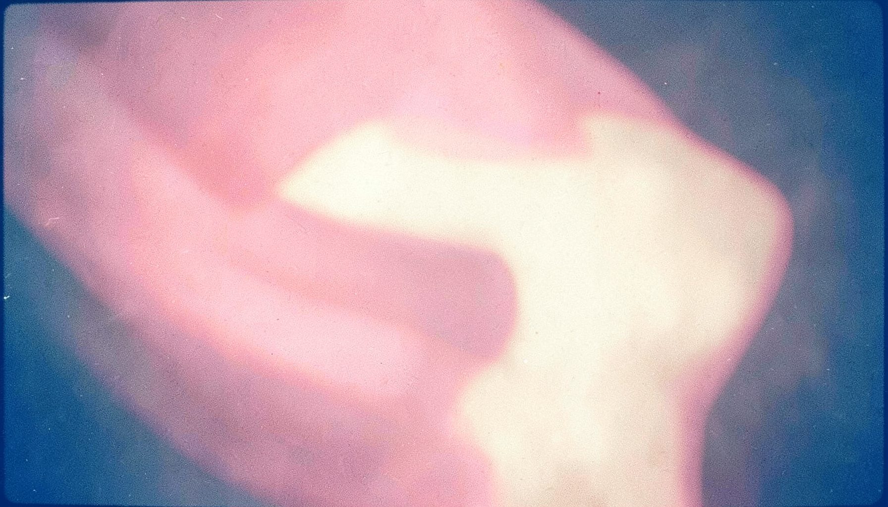 Soft pink and cream abstract organic shapes with a warm, diffused glow, reminiscent of an analog film photograph with visible grain