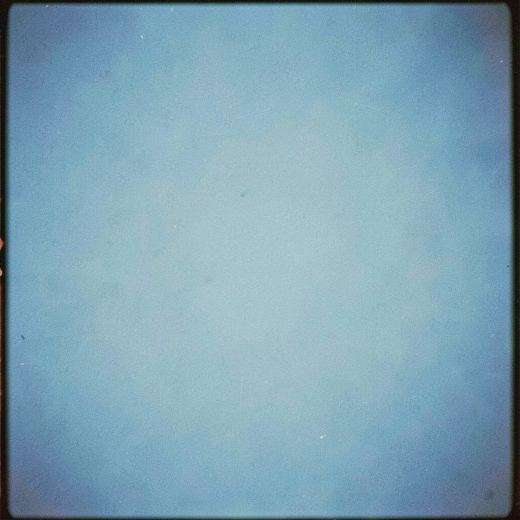 A warm analog film photograph with visible grain, showing soft out-of-focus shapes in creamy white and gentle sky blue, conveying a calm clinical-comfort mood.