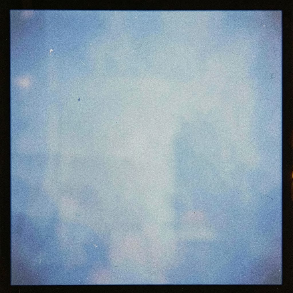 A grainy analog film photograph with a soft, dreamy quality in muted blush and pale blue tones, suggesting comfort and feminine wellness.